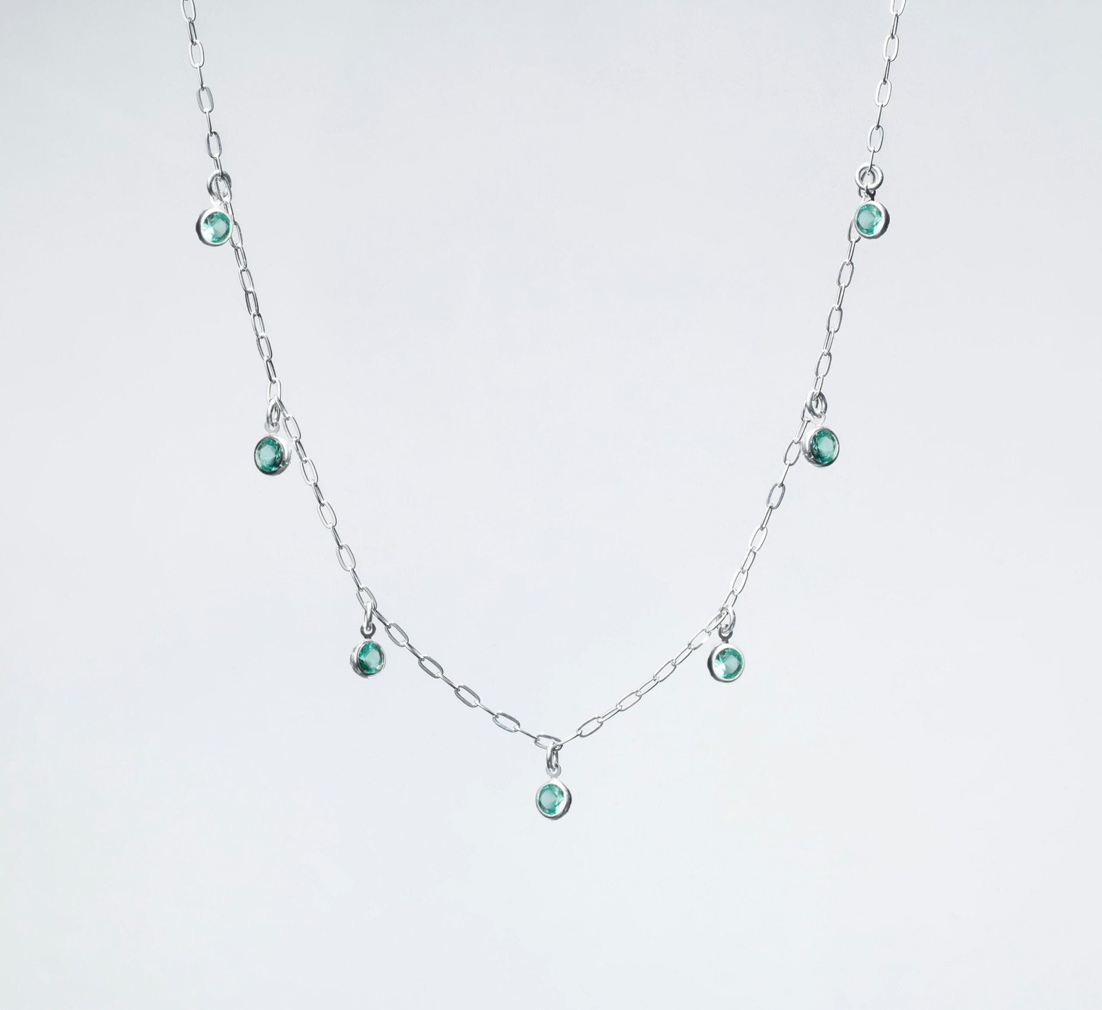 a silver necklace with green beads on a white background